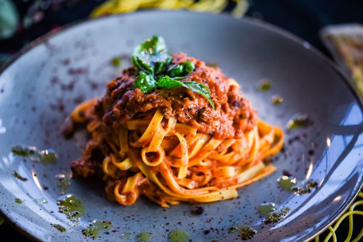 o portie de paste cu Sos Bolognese, pe o farfurie gri, ornată cu câteva picături de ulei și o frunză de busuioc în vârf. Unul din cele mai populare sosuri italiene pentru paste