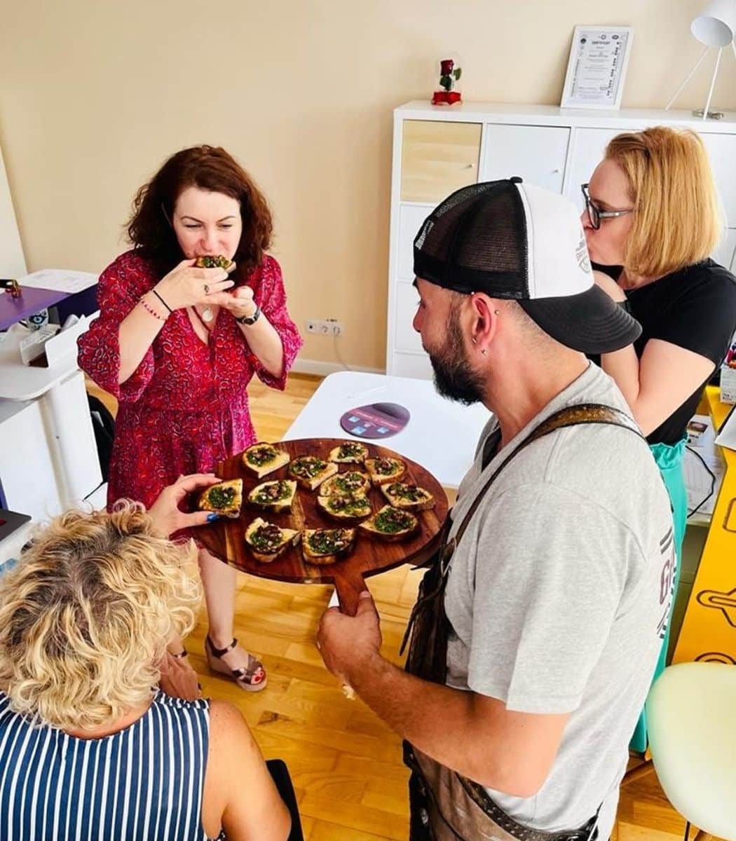 un bucătar on demand servește mai multi oameni cu bruschete de pe un platou vișiniu, in cadrul unei experiente culinare