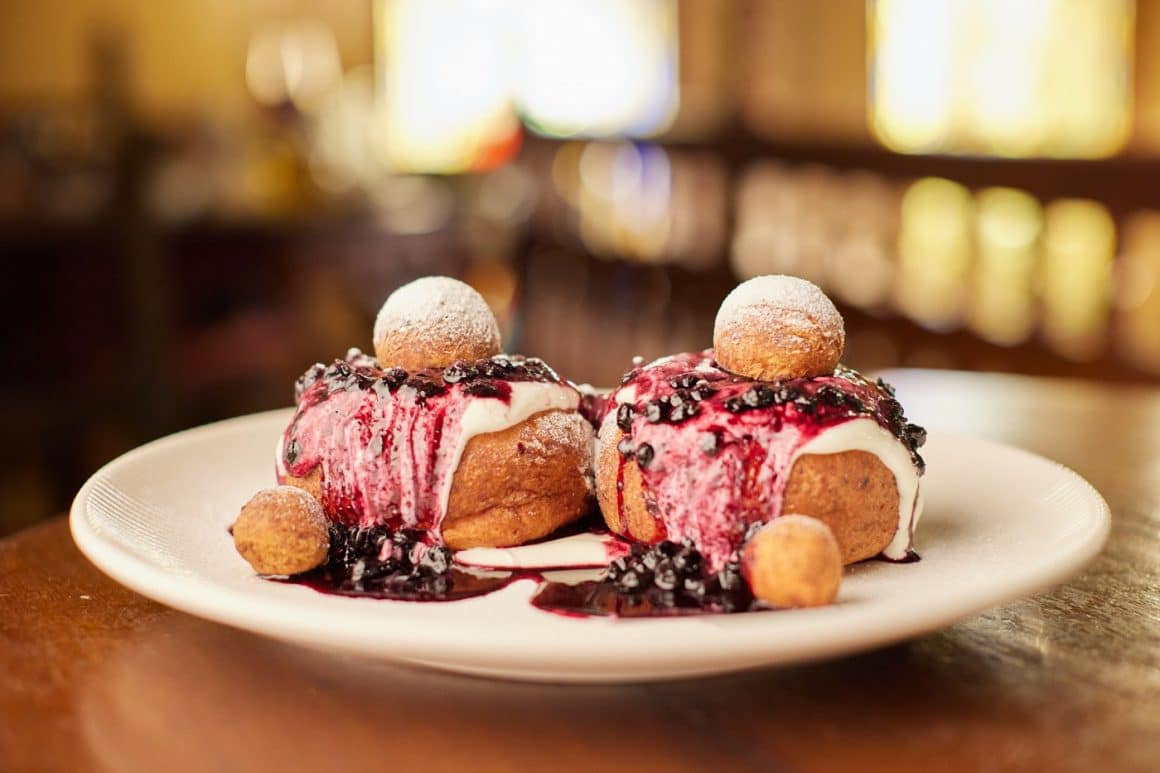 2 papanasi grasuni cu dulceata de afine si smantana, in prim plan, la caru cu Bere București