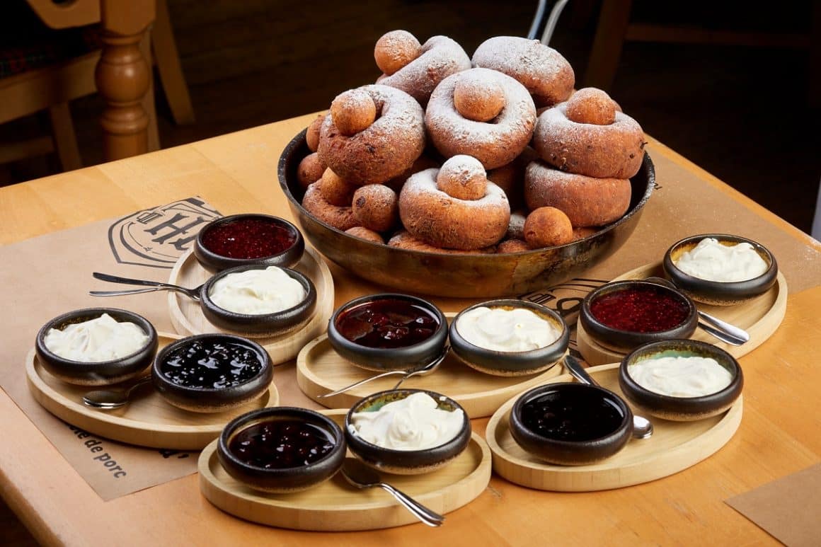 Bol plin cu papanași, iar alturi de ei mai multe boluri cu smantana si dulceata