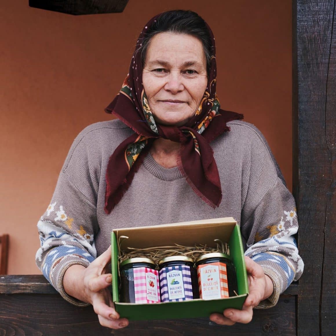 o femeie in vârstă ține în mână o cutie cu trei borcane de zacuscă
