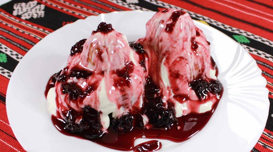 close up cu o farfurie cu 2 papanasi cu smantana si dulceata, asezate pe un stergar rosu cu motive traditionale, de la Vatra restaurant, unde mâncăm papanași buni în București