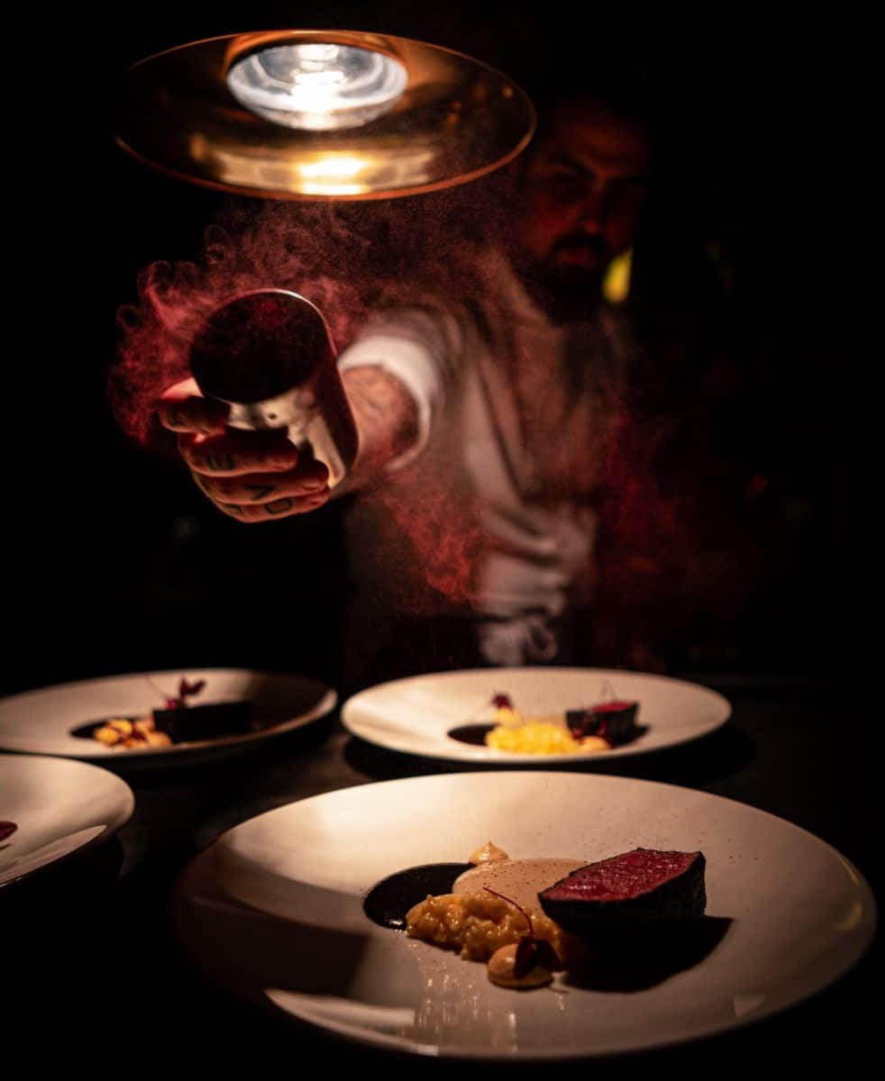 chef Radu Ionescu presara un praf rosu peste 3 farfurii cu steak, in lumina difuza