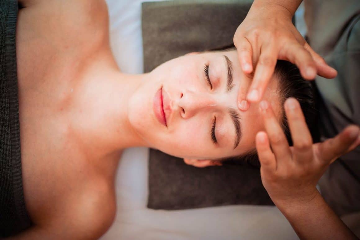 o femeie ii face un masaj facial unei alte felei, ininstă pe o masă de spa în românia