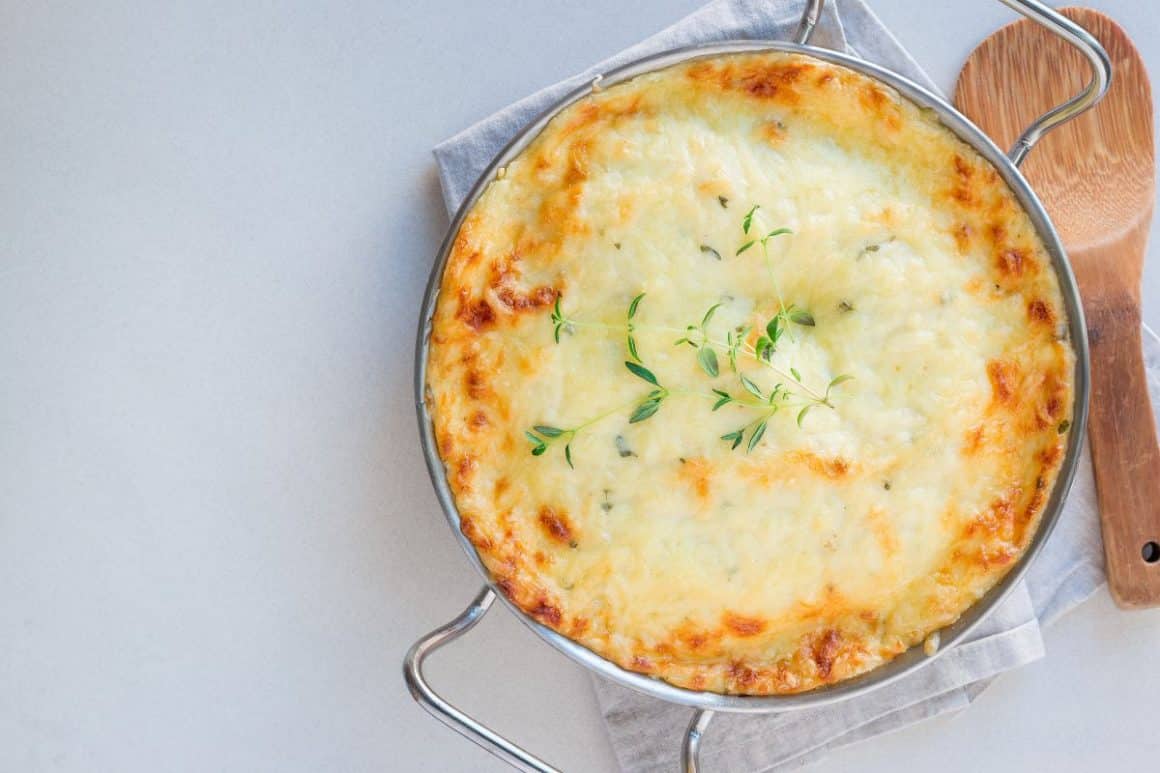 un vas metalic cu mânere este aseszat pe un servet de bucătărie, iar langa el este o lingură de lemn