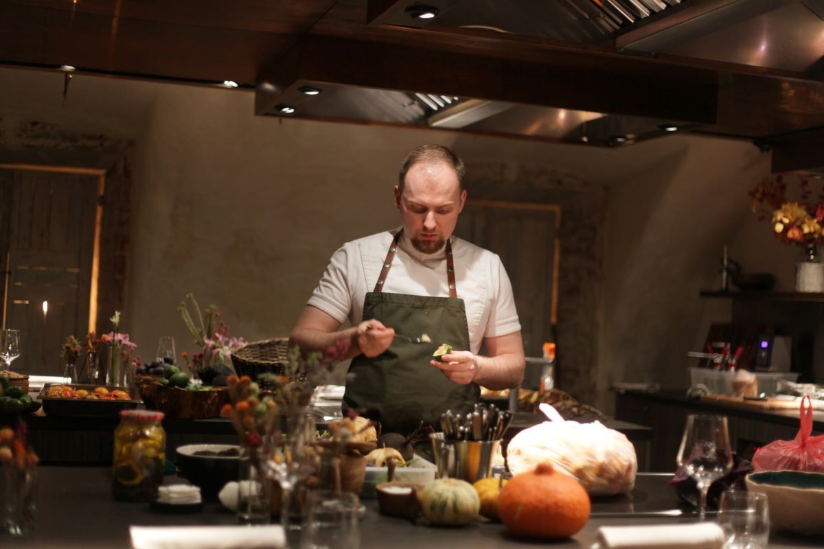 un bucătar personal prepară mai multe feluri de mâncare pe un blat de bucătărie pe care sunt mai multe legume și ustensile de bucătărie