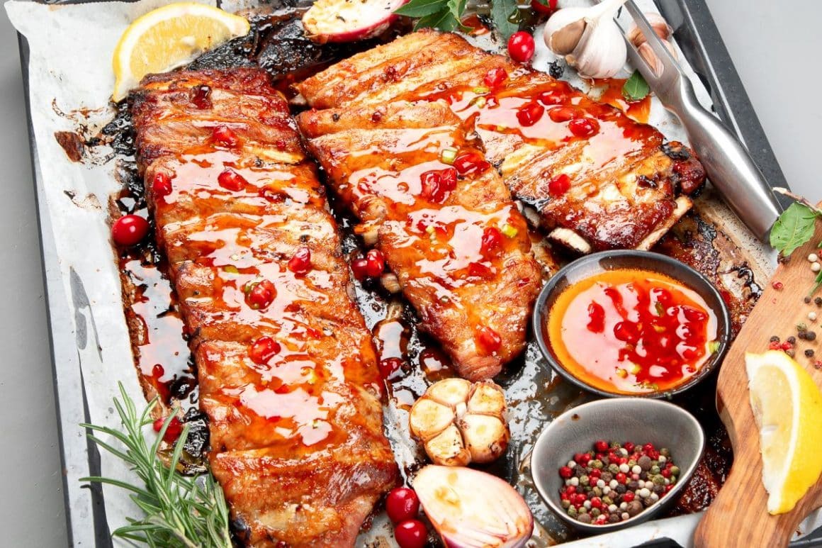 trei bucăti de coaste la cuptor, într-o vatvă,sunt unse cu marinade pentru carne din sos de rodie și boabe de piper