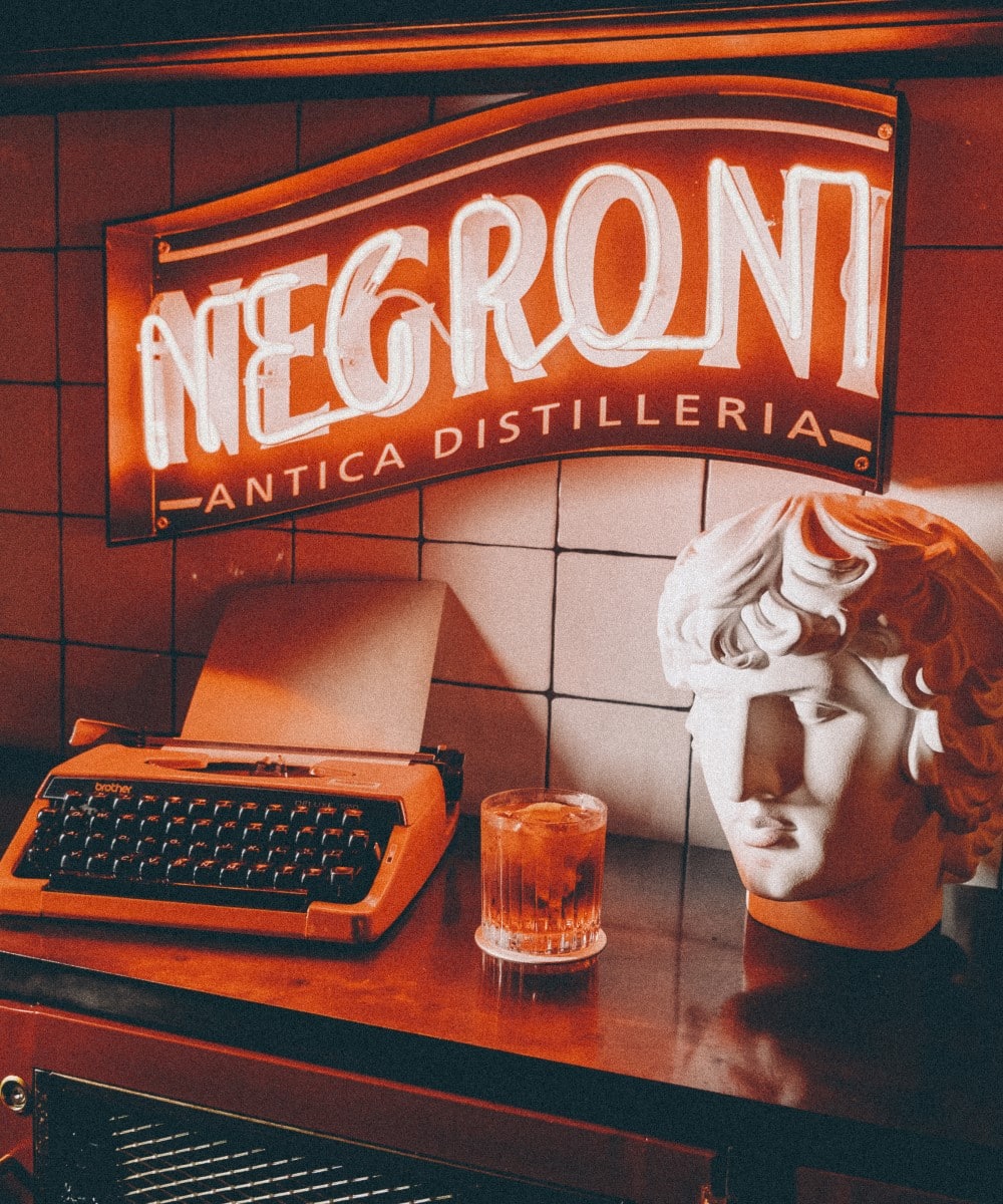 o masina de scris, un pahar de negroni, o statueta si sigla luminoasa negroni