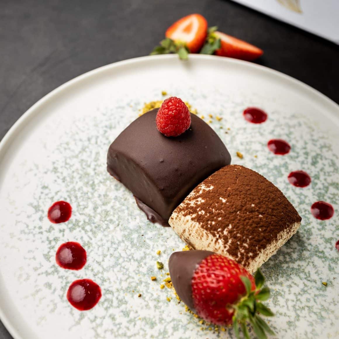 2 prajituri pe o farfurie alaturi de capsuni in ciocolata