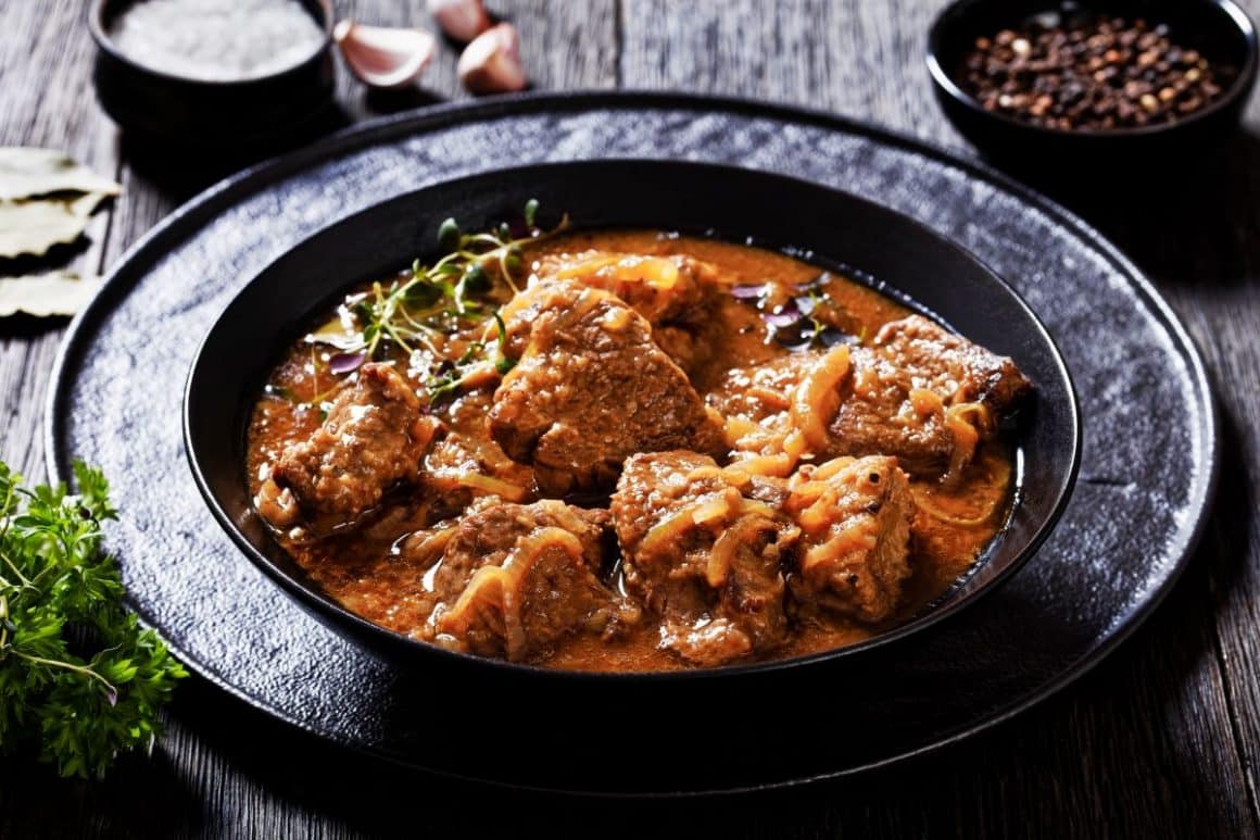 o portie de tocana flamandă servită într-o farfurie neagră, alături de un bol de piper si un altul de sare. De mâncat în Bruges