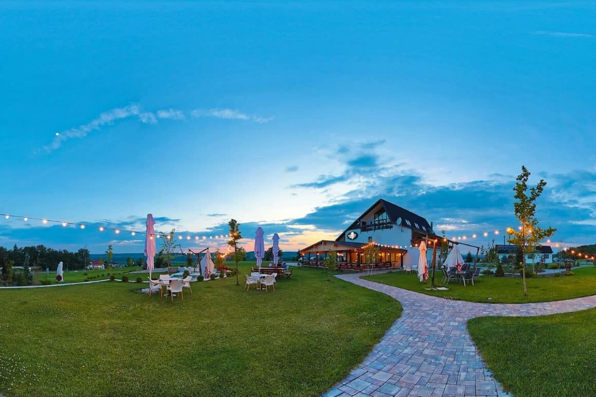 mai multe mese sunt asezate pe peluza cu gazon a unei locații spa din România, la apus. Forest Retreat