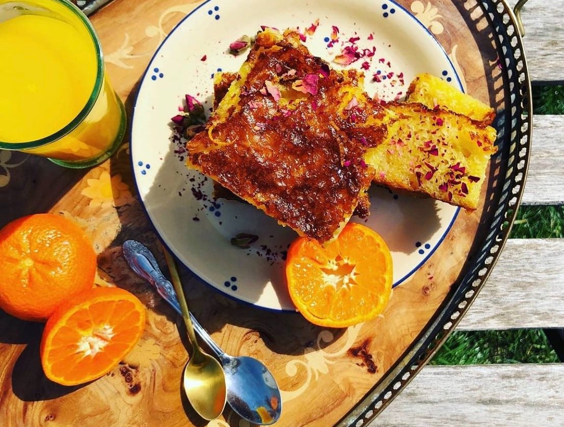 farfurie cu portokalopita fotografiata de sus, asezata pe o tava alaturi de portocale si suc de portocale