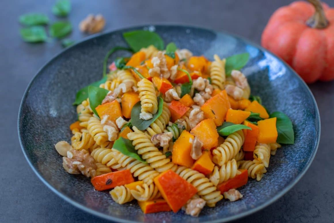 o portie de paste cu dovleac plăcintar și verdeata este asezata pe o faarfurie modernă, bleumarin