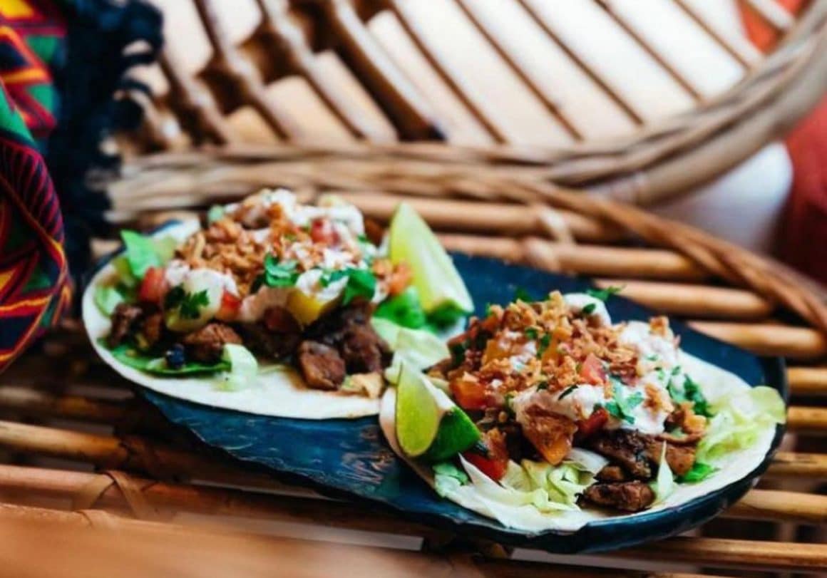 2 tacos serviti pe un platou, cu carne si legume asezate pe tortilla de porumb