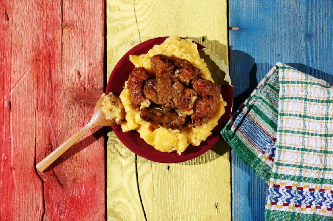 o porție de cârnați din bucătăria tradițională românească fotografiata pe o masă pictată în culorile steagului româniei și un ștergar tradițional