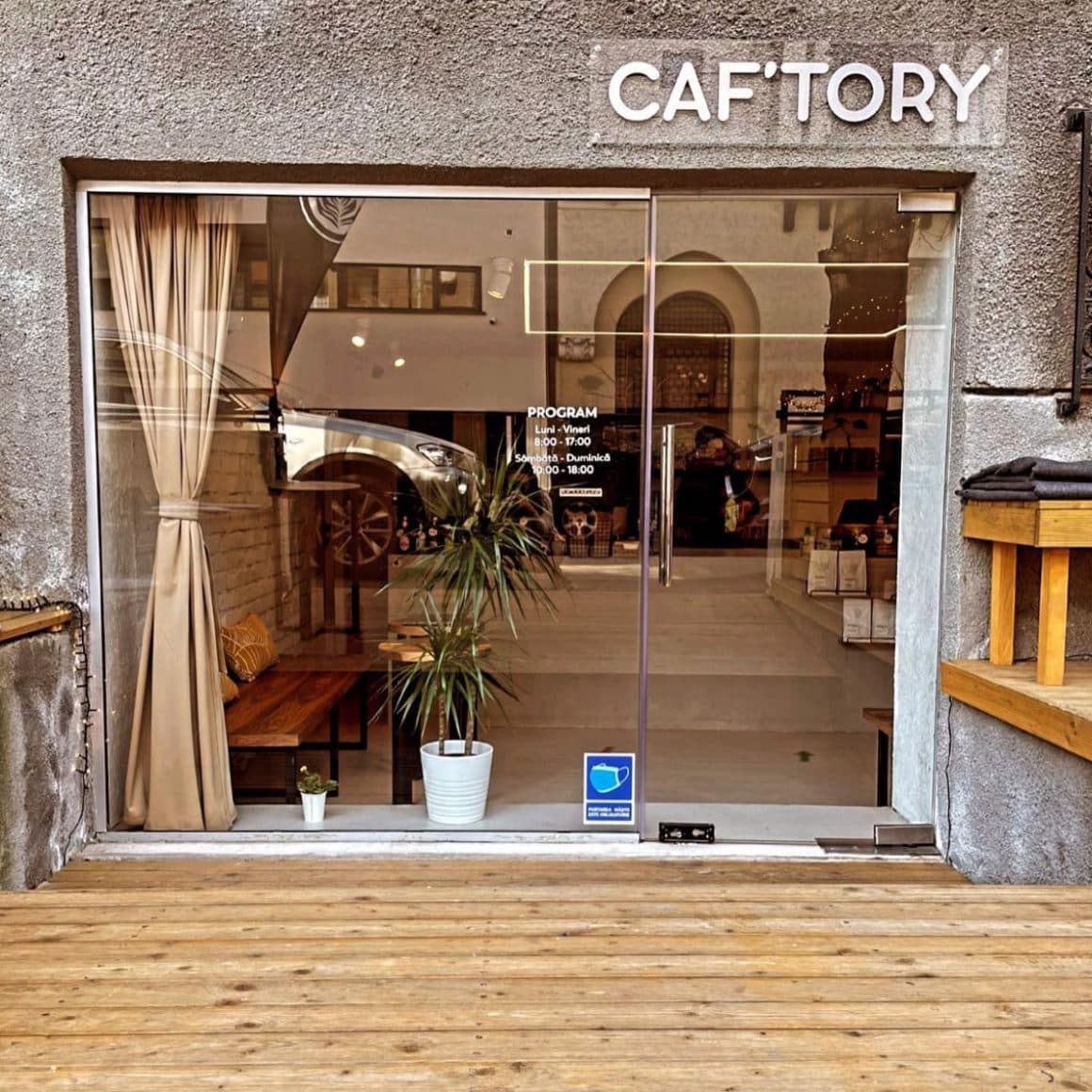 intrarea cu geamuri mari într-o cafenea micuță din bucurești, cu o draperie crem șiun ghiveci alb