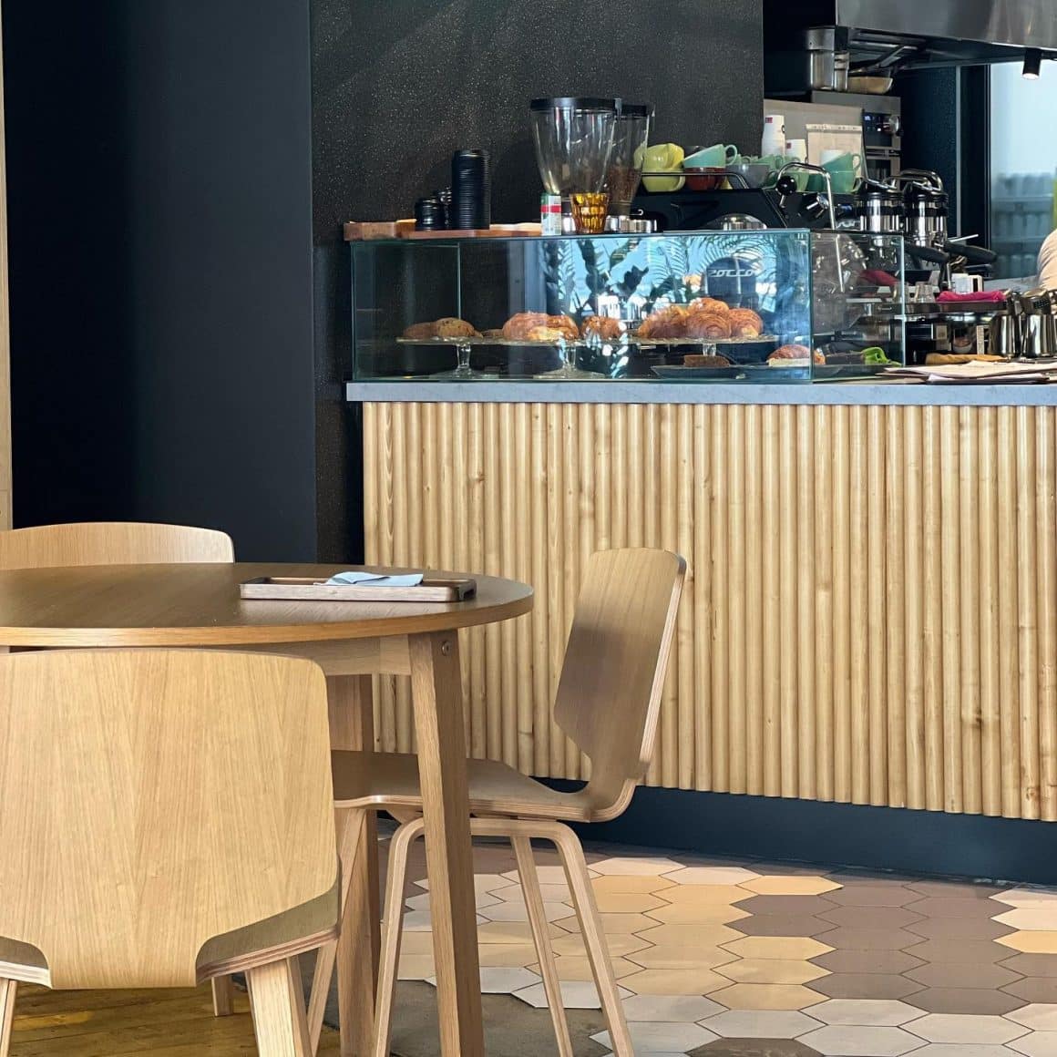 masa din lemn in fata unui bar tot din lemn si in fundal un perete negru la cafeneaua M60