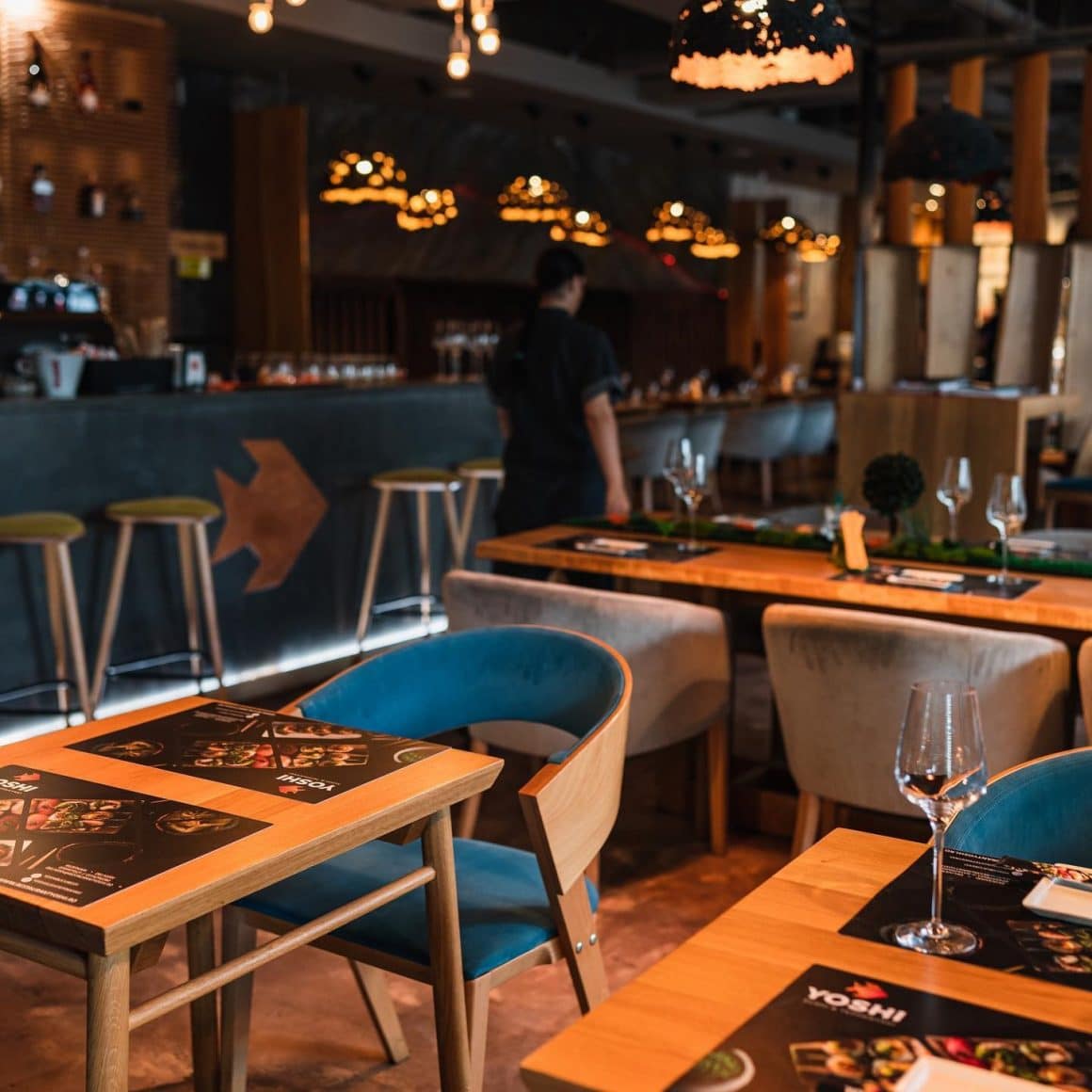 prim plan cu o masă de 2 peroane la restaurant Yoshi Sushi, iar in fundal, blurat, restaurantul iluminat discret