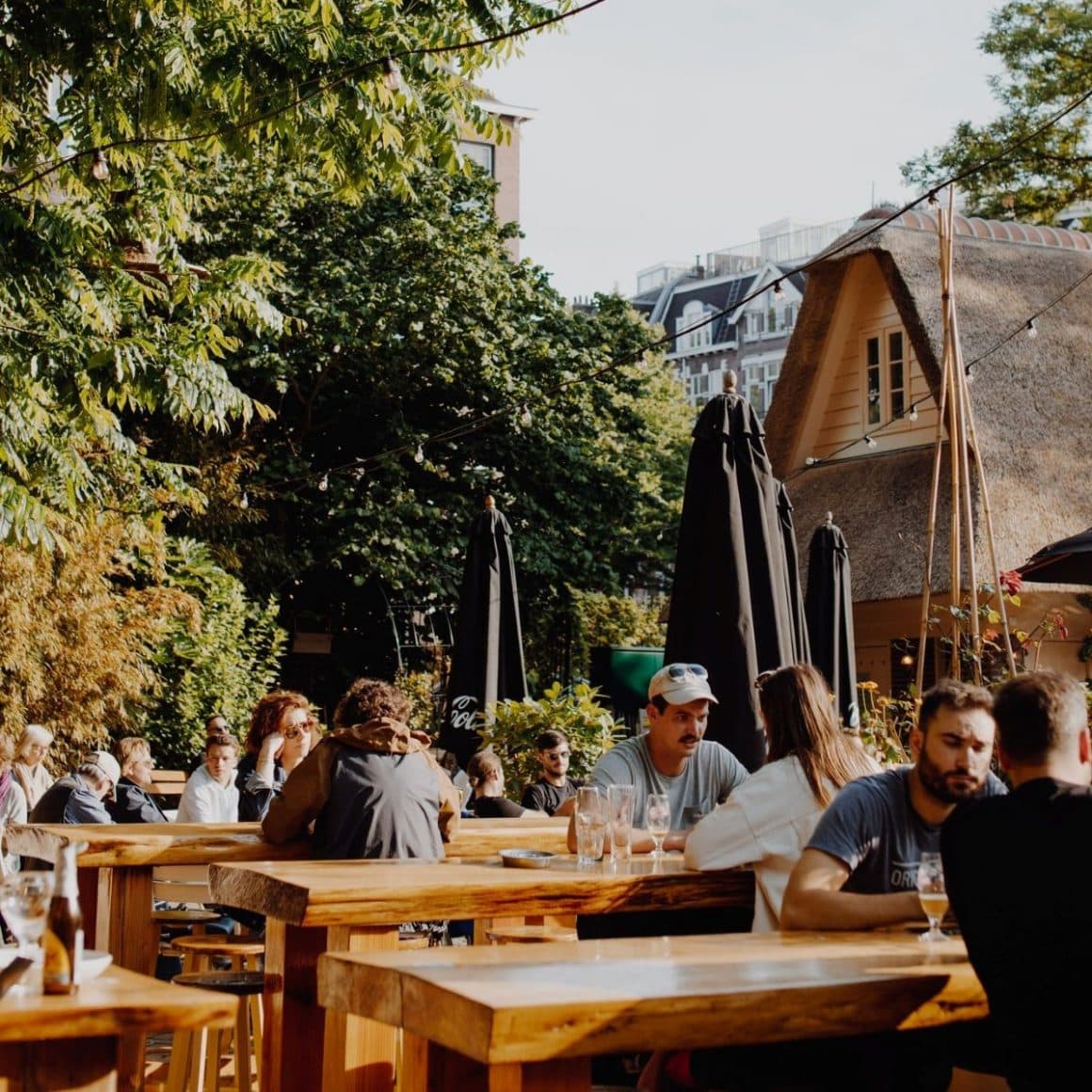 mai multi oameni iau masa sau beau un pahar la una dintre terasele dintr-un parc din amsterdam