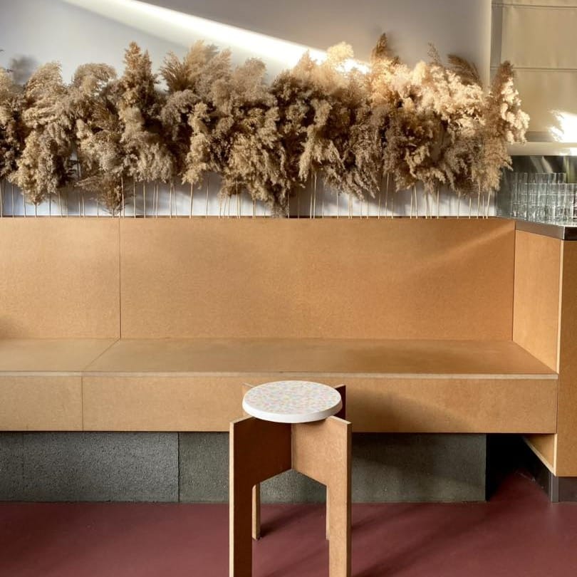 mai multe buchete de iarbă uscată sunt puse la uscat deasupra unei canapele de lemn dintr-o cafenea