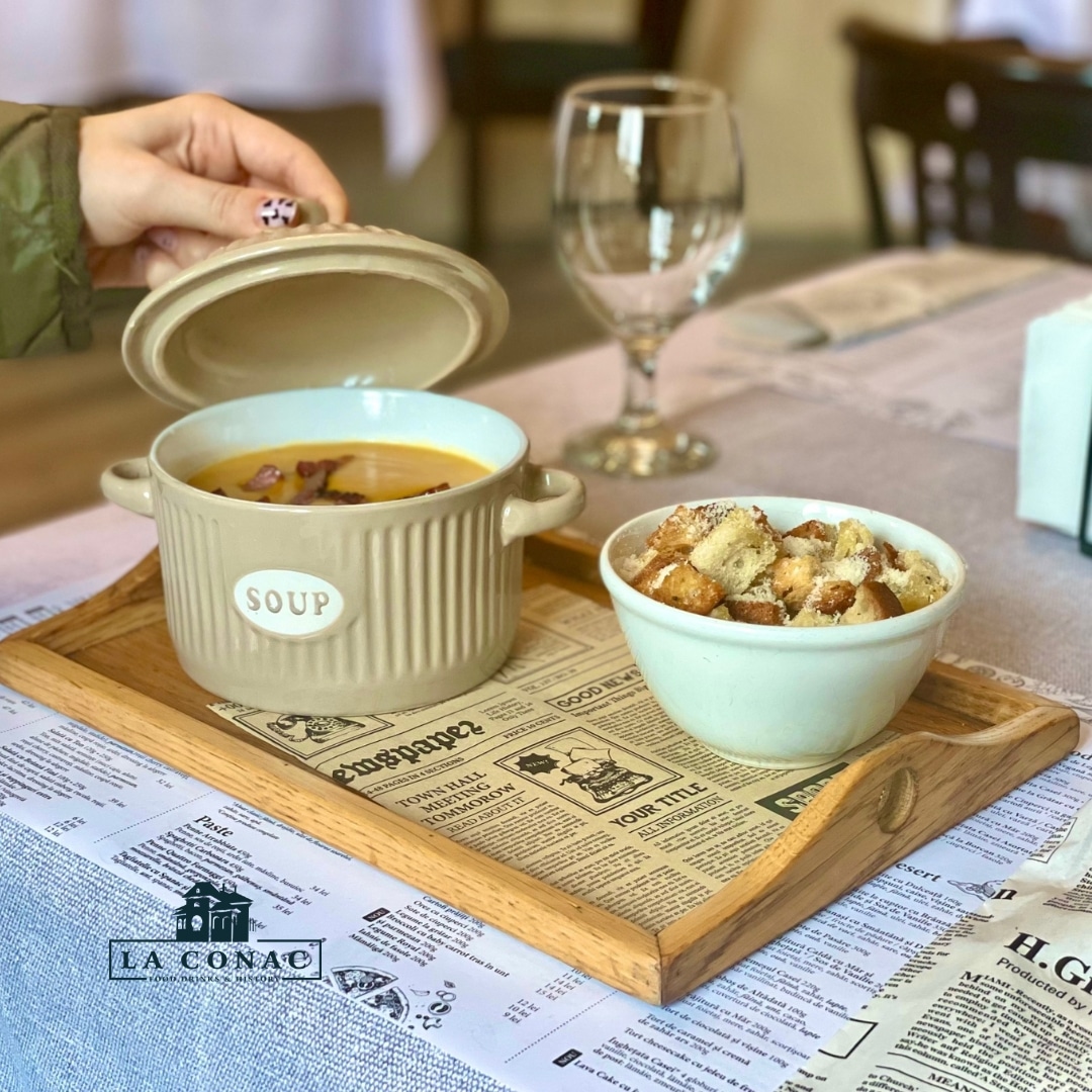 o femeie ridică un capac al unei oale de teracotă, pe un platou de servire de lemn