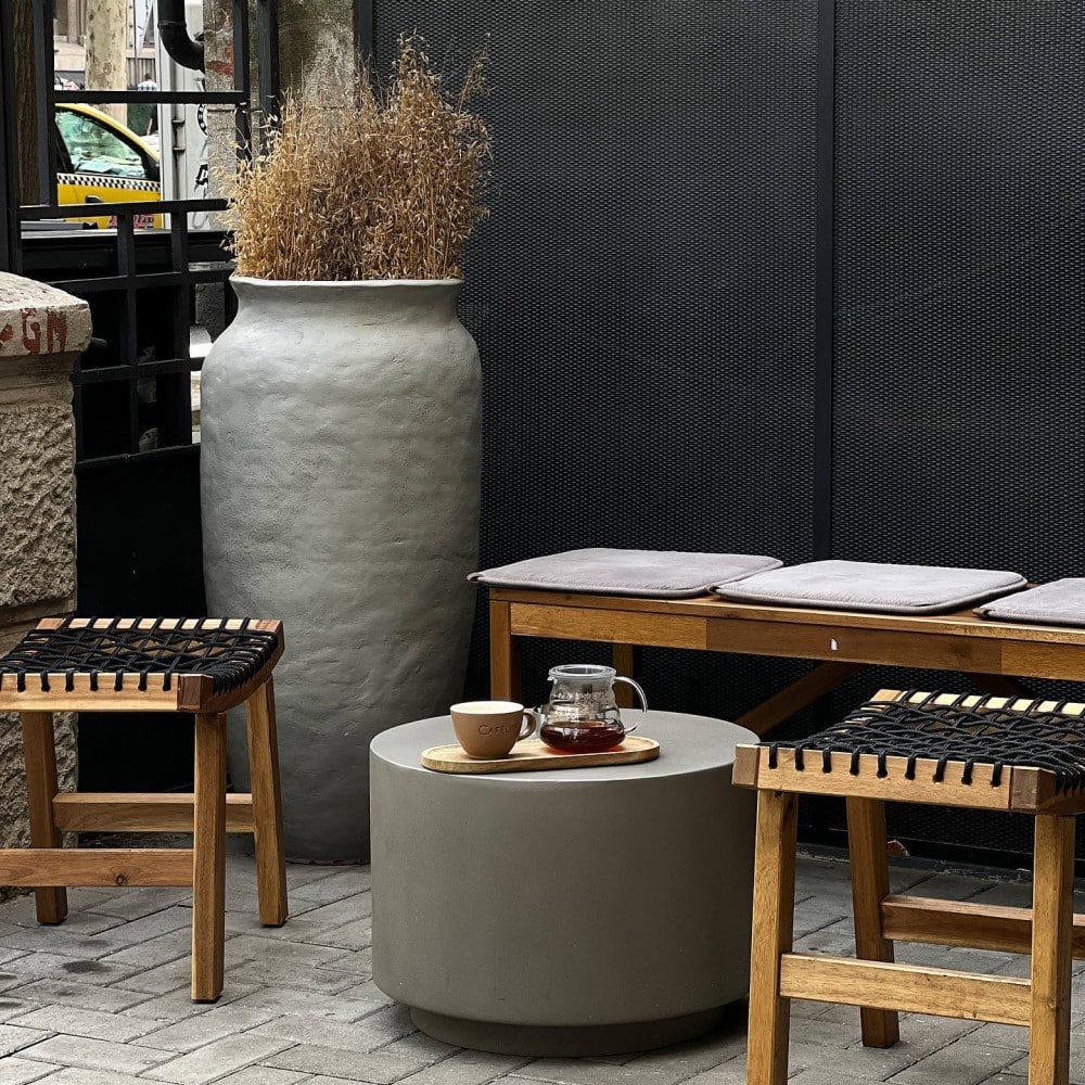 mobilierul unei cafenele micuțe din bucurești, cu scaune de lemn, o măsuță circulară și un ghivechi amre, din piartă