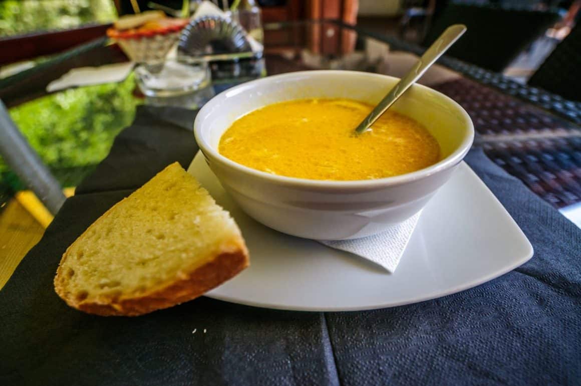 un bol alb cu ciorbă de burtă este asezat pe o farfurie intinsă, alături de o felie de pâine