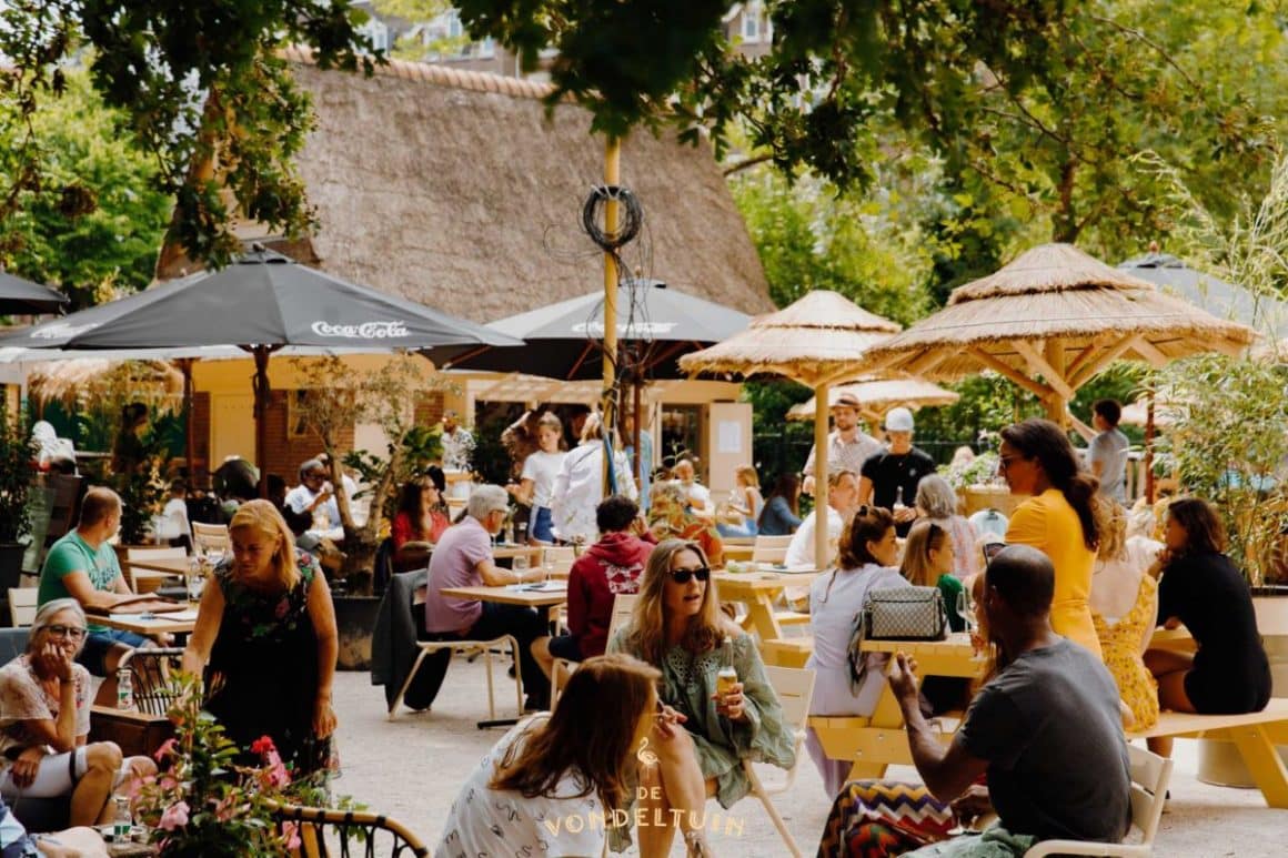 mai multi oameni iau masa sau beau un pahar la una dintre terasele dintr-un parc din amsterdam