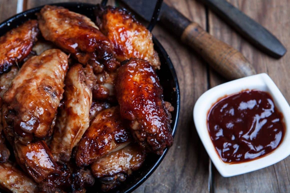 mai multe aripioare picante intr-o farfurie, alături de un bol mic cu sos barbecue pentru mancaruri picante