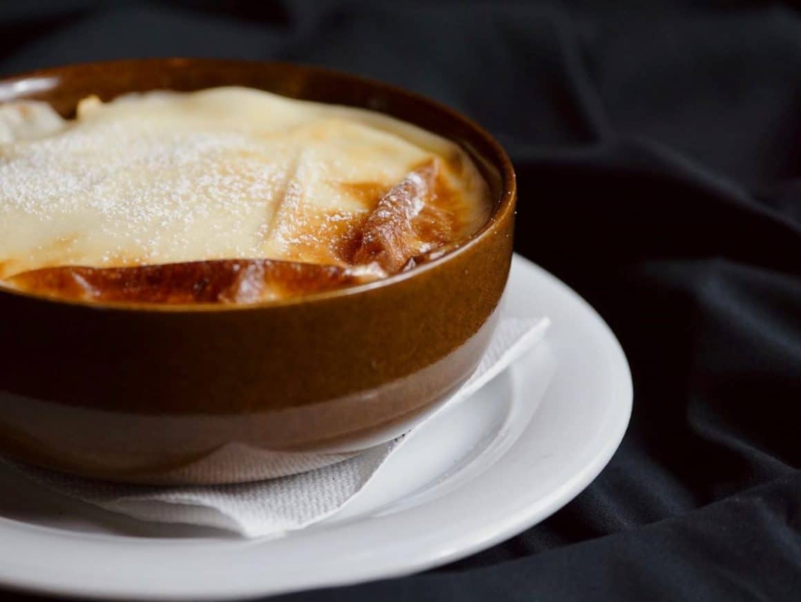 o porție de mâncare scoasă din cuptor este servită pe o farfurie neagră, într-un restaurant din alba iulia, alături de o sticlă de vin