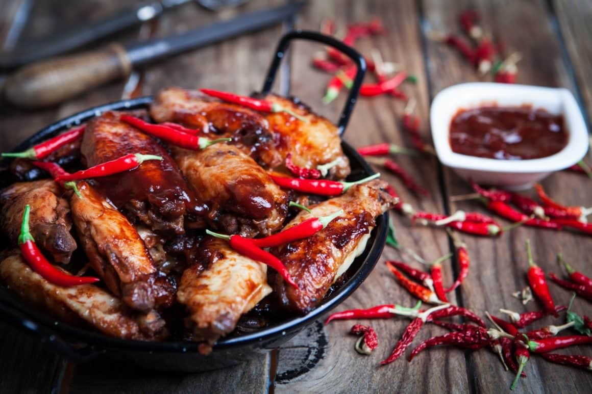 close up cu o portie de aripioare picante intr-o farfurie, iar pe langa multi ardei iuti rosii