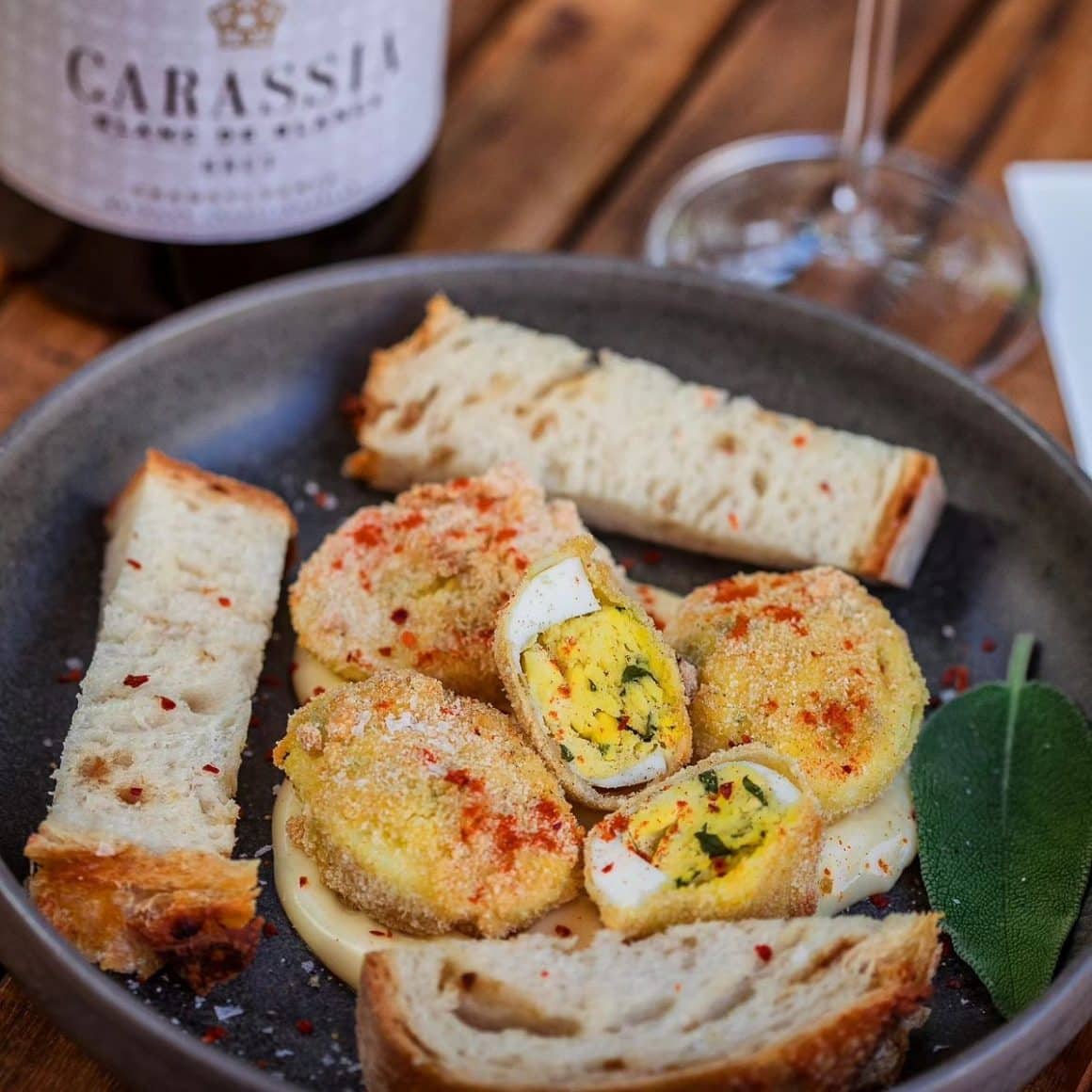 o porție de ouă franțuzite, cu câteva bucăți de pâine pe o farfurie, alături de o sticlăși un pahar de vin