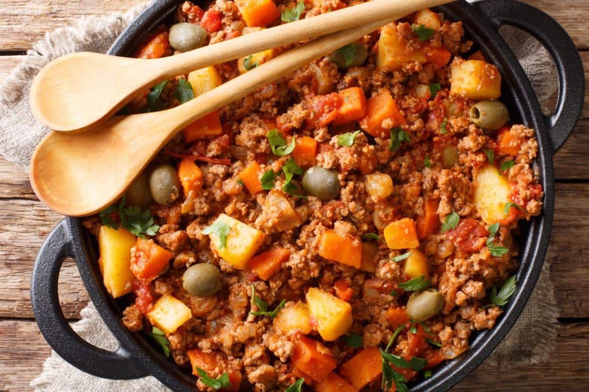 o oală de fontă cu picadillo, unul din felurile de mancăruri picante mexicane, cu două linguri de lemn deasupra