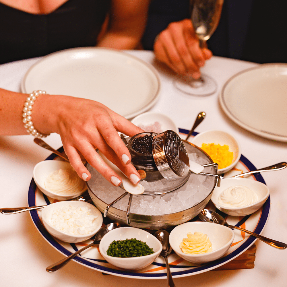 o femeie ia cu mâna un recipient cu icre negre de pe un platou