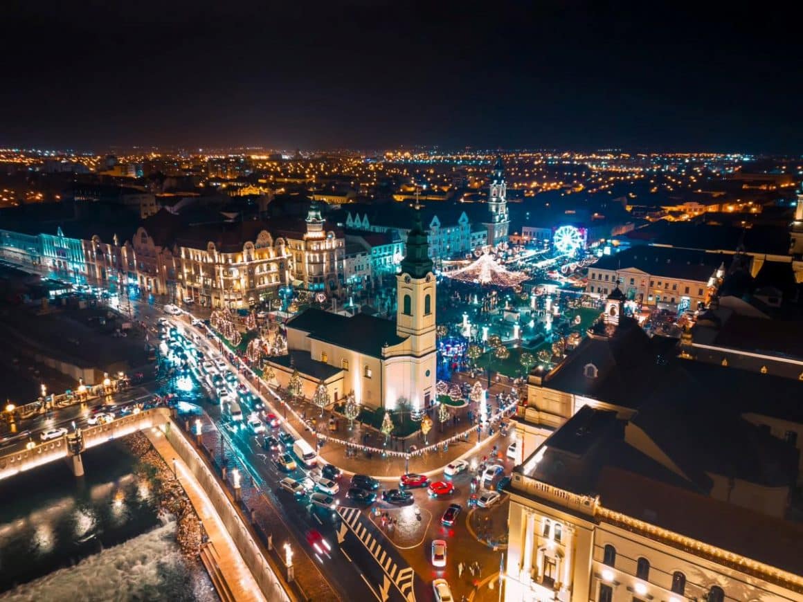 o fotografie aeriana cu casutele de la targul de craciun din oradea și cateva cladiri emblematice pentru oras, luminiate de beculetele de la targul de crăaciun
