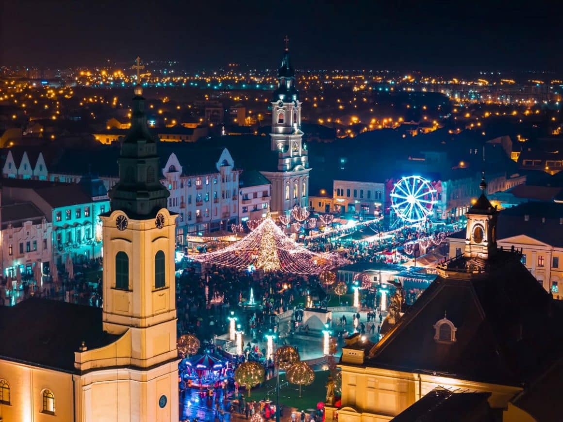 o fotografie aeriana cu casutele de la targul de craciun din oradea și cateva cladiri emblematice pentru oras, luminiate de beculetele de la targul de crăaciun