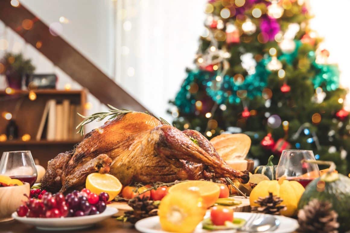 friptură de Crăciun din curcan, asezata pe o masa bogata, iar in fundal bradul impodobit