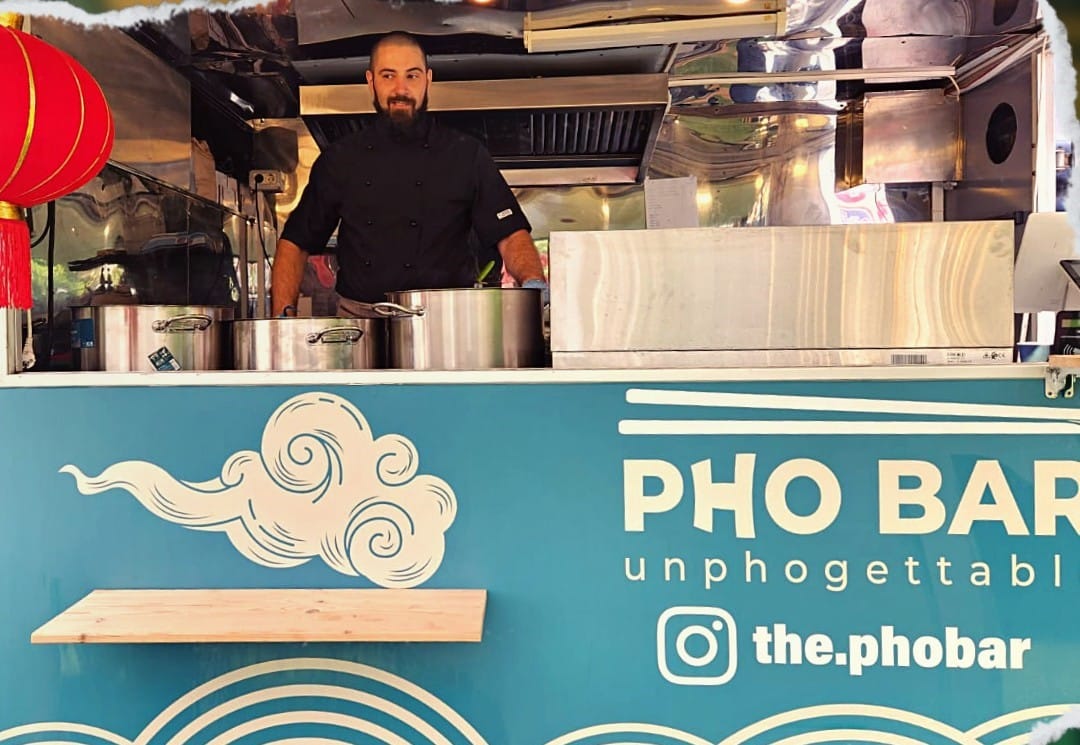 un barbrat pozează în interiorul unui food truck, la un festival gastronomic. Cele mai bune food trucks