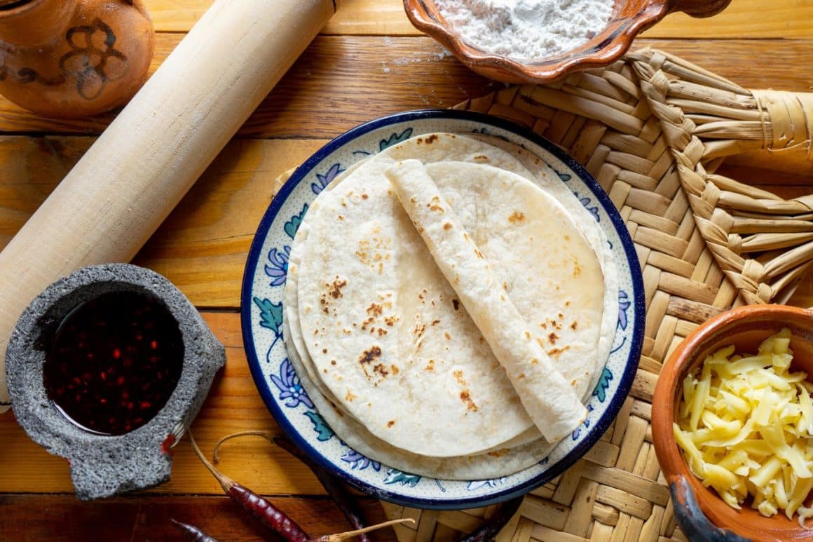 mai multe tortilla sunt asezate pe o masă, alături de alte ingrediente mexicane. Ce poți face cu tortilla