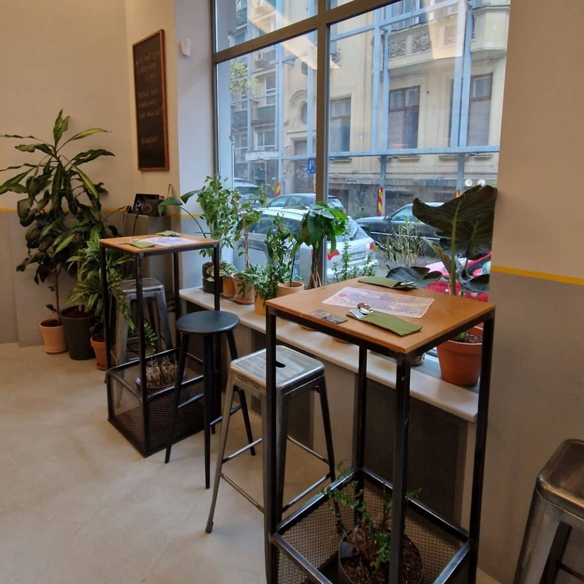 mese inalte cu scaune de bar asezate in fata unei ferestre mari la Dumicat București.