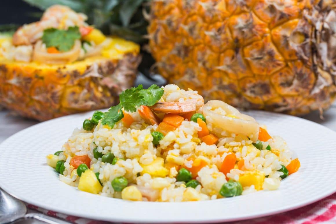 o farfurie cu mai multe ingrediente folosite la prepararea unei salate calde salate calde, alături de un anana umplut cu orez