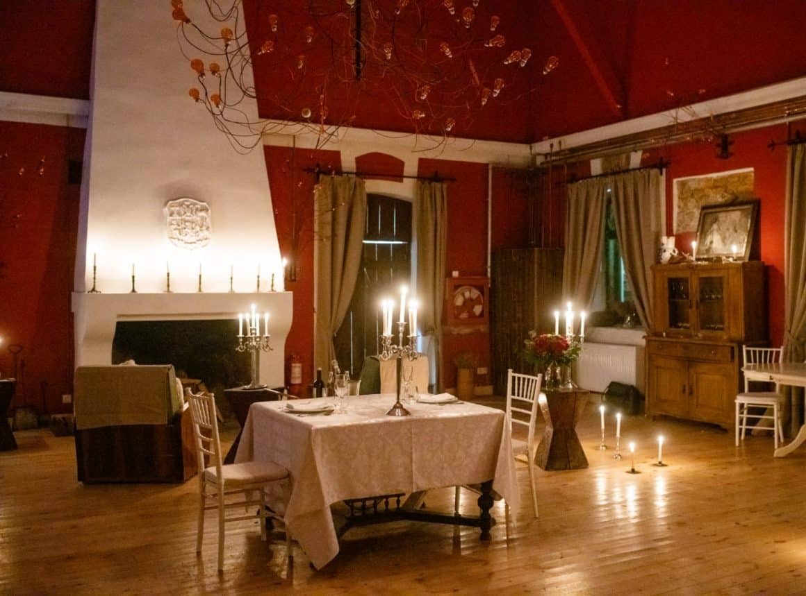 o masa de 2 persoane, in fata unui semnieu alb, intr-o incapere rosie, deocrata cu lumanari, la zabola estate - una din destinații romantice din România