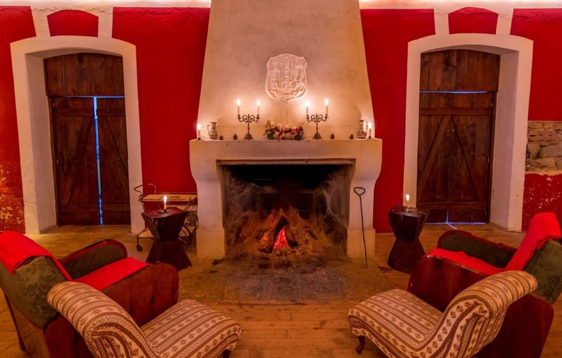 2 fotolii in fata unui semineu, alb , pe fundal rosu, cu lumanari aprinse