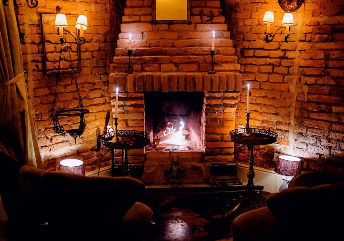 2 fotolii in fata unui semineu din caramida, aprins, decorat cu lumanari