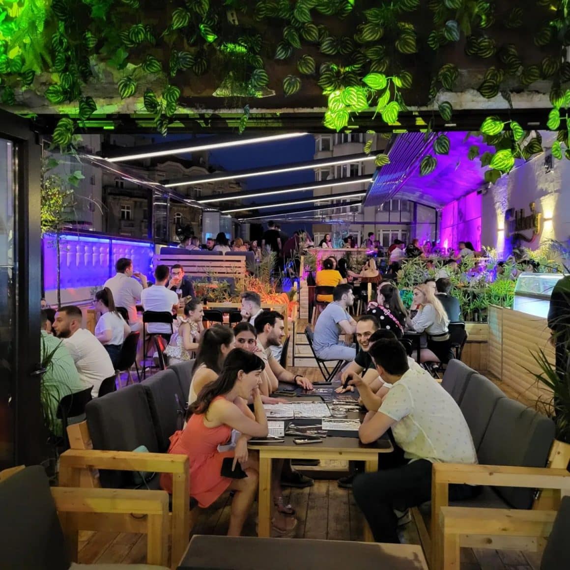 Oameni asezati la mese si la bar pe terasa la Balkon Resto Garden, unul din restaurante la înălțime din București