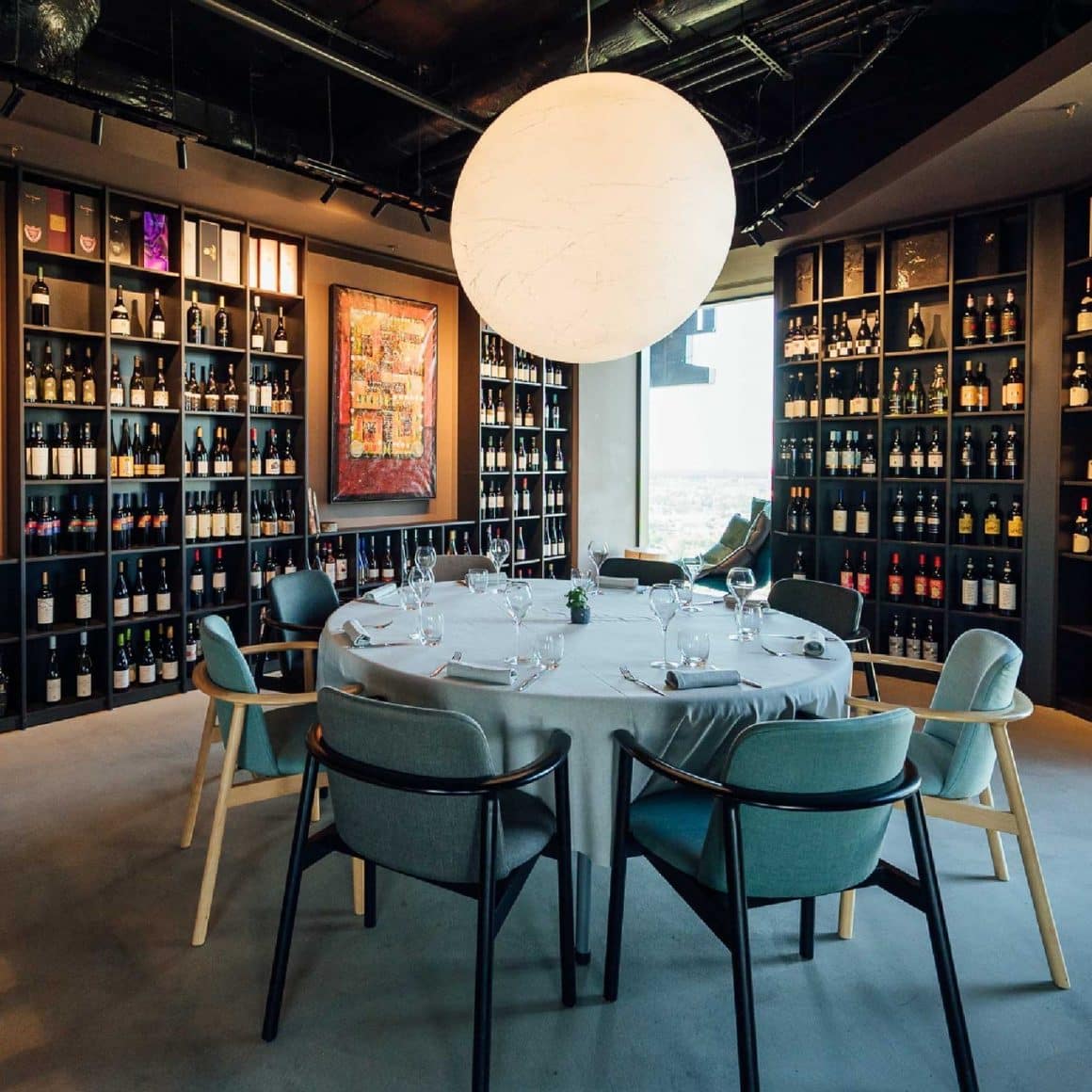 masa rotunda amplasata in vinoteca de la Fork Ana Tower, cu dulapuri mari cu sticle de vin in stanga si dreapta