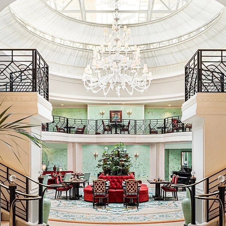 Imagine de ansamblu din restaurant La Bauhinia din Paris, situat sub o cupola mare de sticla, cu un candelabru imens din cristal atarnat in mijloc, pereti verzi si mobilier elgant, cu rosu.