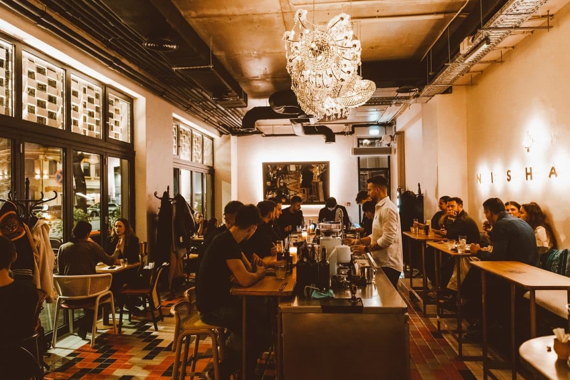 mai multi oameni care iau masa le restaurant Nishani din Bucuresti, cu barul in centrul incaperii si mese de o parte si de alte. Restaurante 1 martie