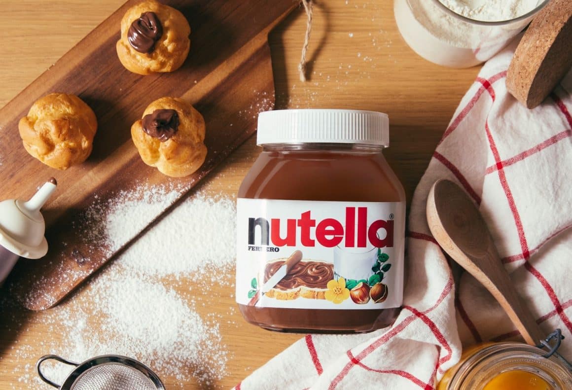 Un borcan de nutella pe o masa, fotografiat de sus, alaturi de niste prajituri