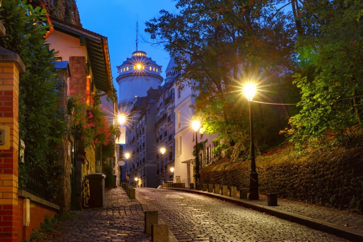 Straduta pavata din cartierul Montmartre, fotografiata seara, cu luminile aprinse pe strada.
